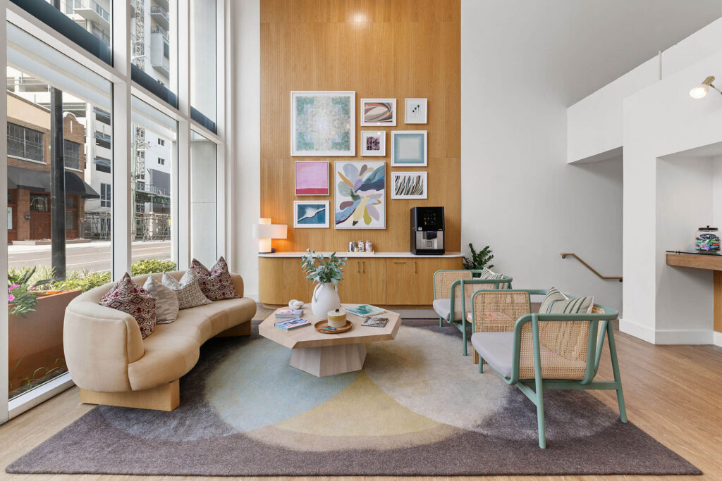 Modern lobby with a curved beige sofa, two chairs, a geometric coffee table, art on a wood accent wall, and large windows letting in natural light.