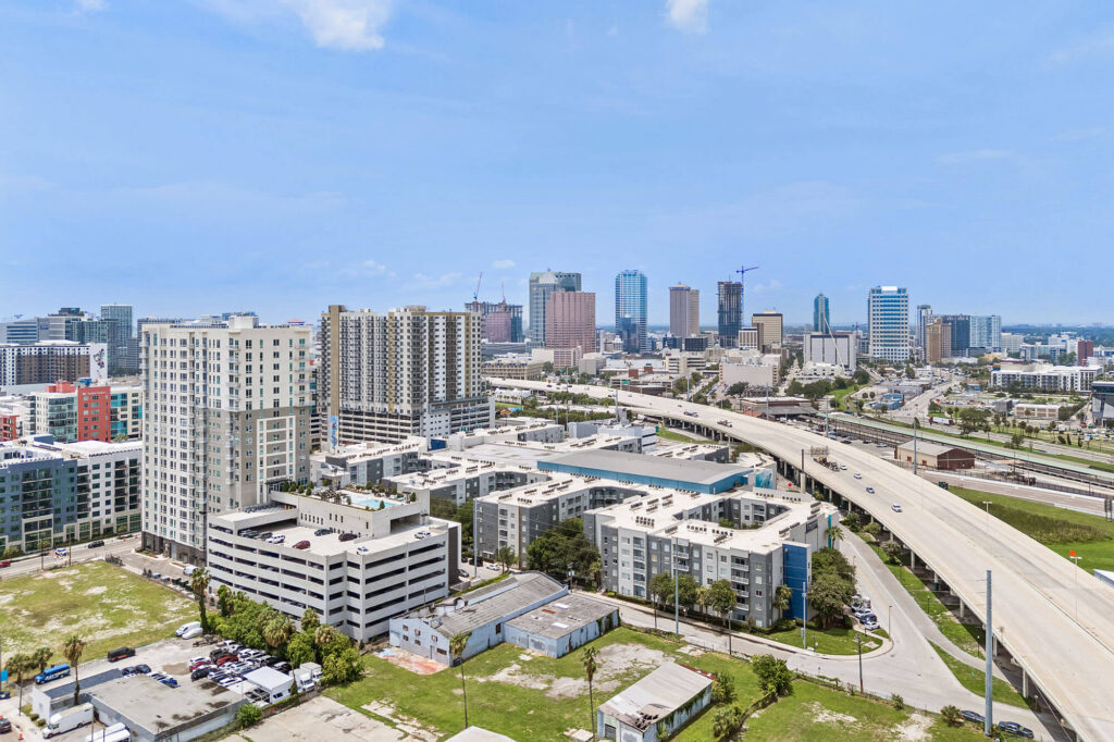 Aerial view of a city skyline with tall buildings, highways, and residential complexes under a clear, blue sky.